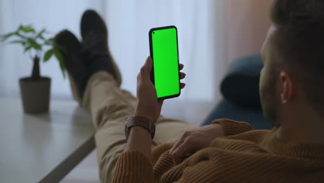 smartphone-with-green-screen-in-hands-of-relaxed-man-in-home-user-is-browsing-internet-site-and-social-nets-reading-e-book-chroma-key-technology